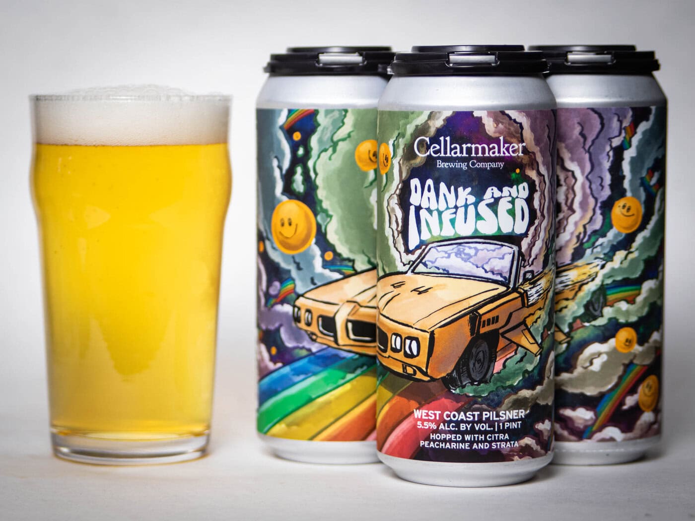 A Glass Of Hazy Beer Sits Beside Three Cans Labeled “Dank And Infused” With Colorful Artwork Featuring A Car, Rainbows, Smiley Faces, And Clouds. The Cans Are From Cellarmaker Brewing Company.
