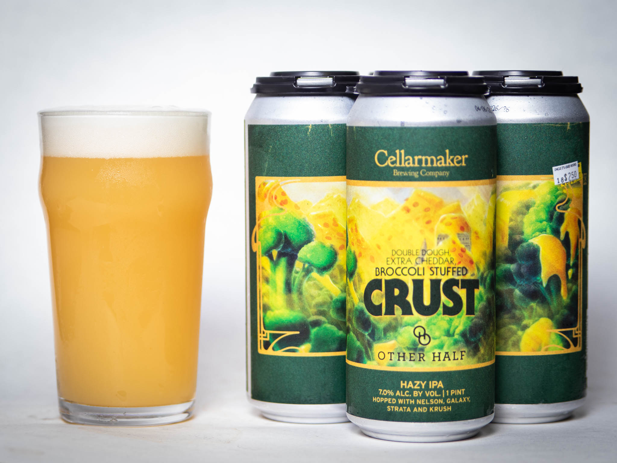 A Glass Of Hazy, Light Yellow Beer Sits Next To Four Cans Labeled “Cellarmaker Brewing Company Double Dough Extra Cheddar Broccoli Stuffed Crust Hazy Ipa.” The Cans Feature Green And Yellow Artwork.