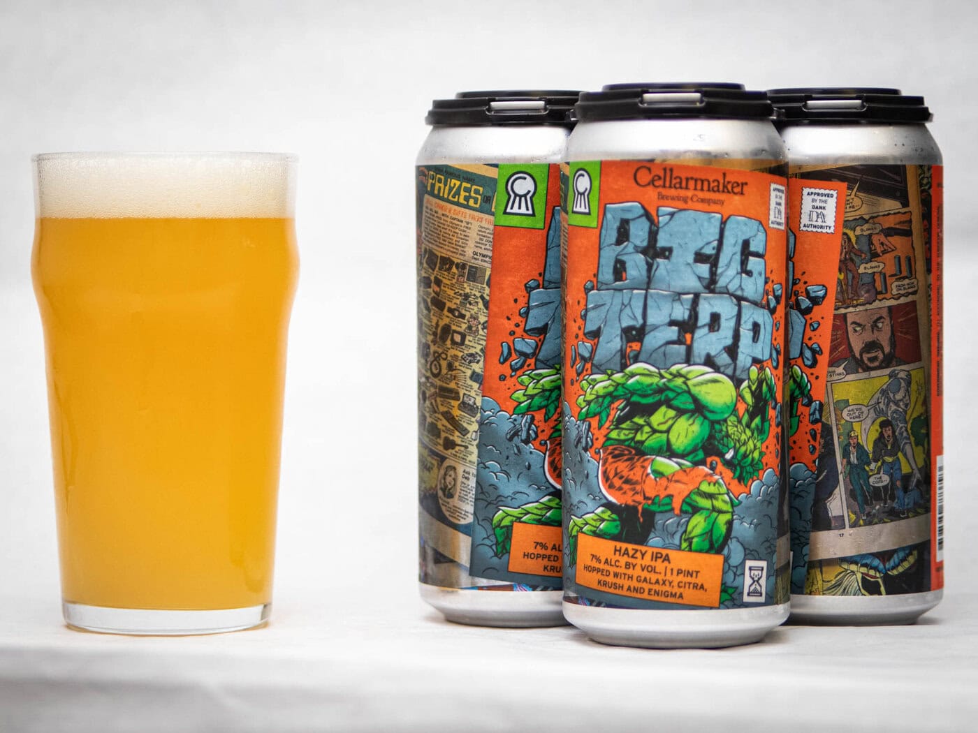 A Pint Glass Filled With Hazy, Golden Beer Sits Next To Four Cans Of Cellarmaker Brewing Co.'S &Quot;Mega Fluff&Quot; Hazy Ipa, Featuring Colorful, Comic Book-Style Artwork On The Cans.
