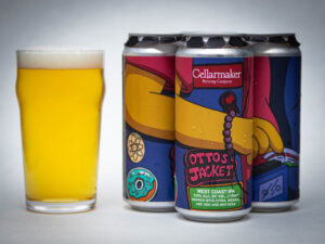 A pint glass of hazy golden beer stands next to three cans of Cellarmaker Brewing Company’s Otto’s Jacket West Coast IPA, featuring colorful, cartoon-style artwork on the labels.