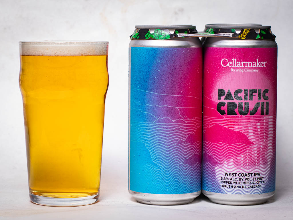 A Pint Glass Filled With Golden Beer Next To Two Cans Of Cellarmaker Pacific Crush West Coast Ipa.