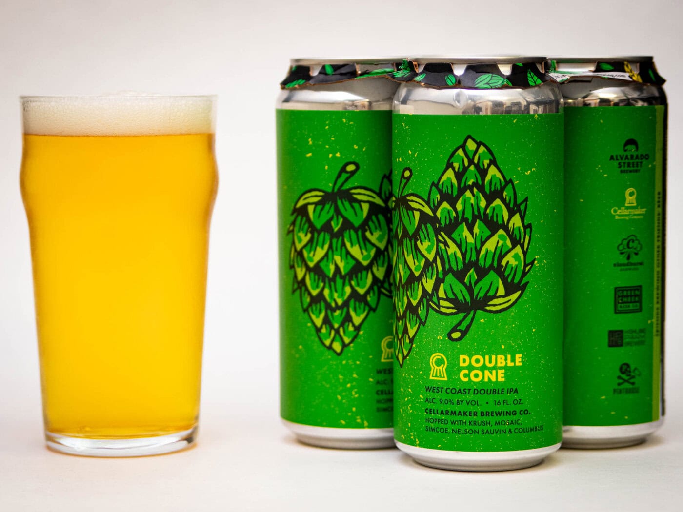 A Glass Of Pale, Hazy Beer Sits Beside Three Green Cans Labeled &Quot;Double Cone&Quot; With Hop Illustrations And Text Indicating It'S A West Coast Double Ipa From Alvarado Street Brewery.