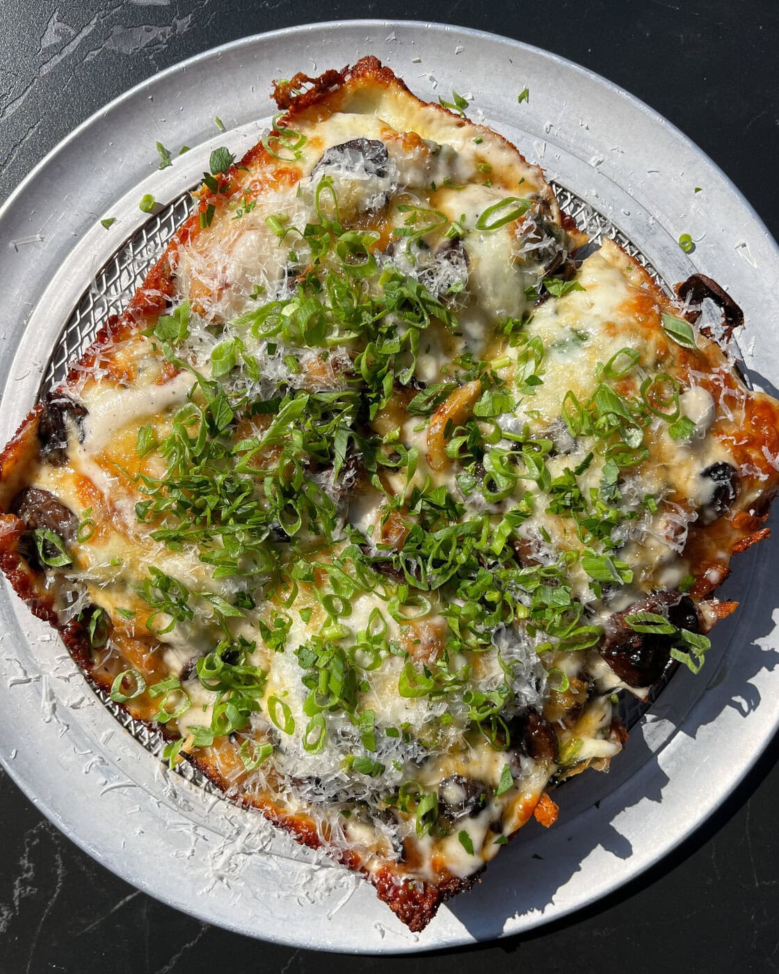 A Rectangular Pizza Topped With Melted Cheese, Sliced Mushrooms, And A Generous Amount Of Chopped Green Onions, Served On A Round Metal Tray.