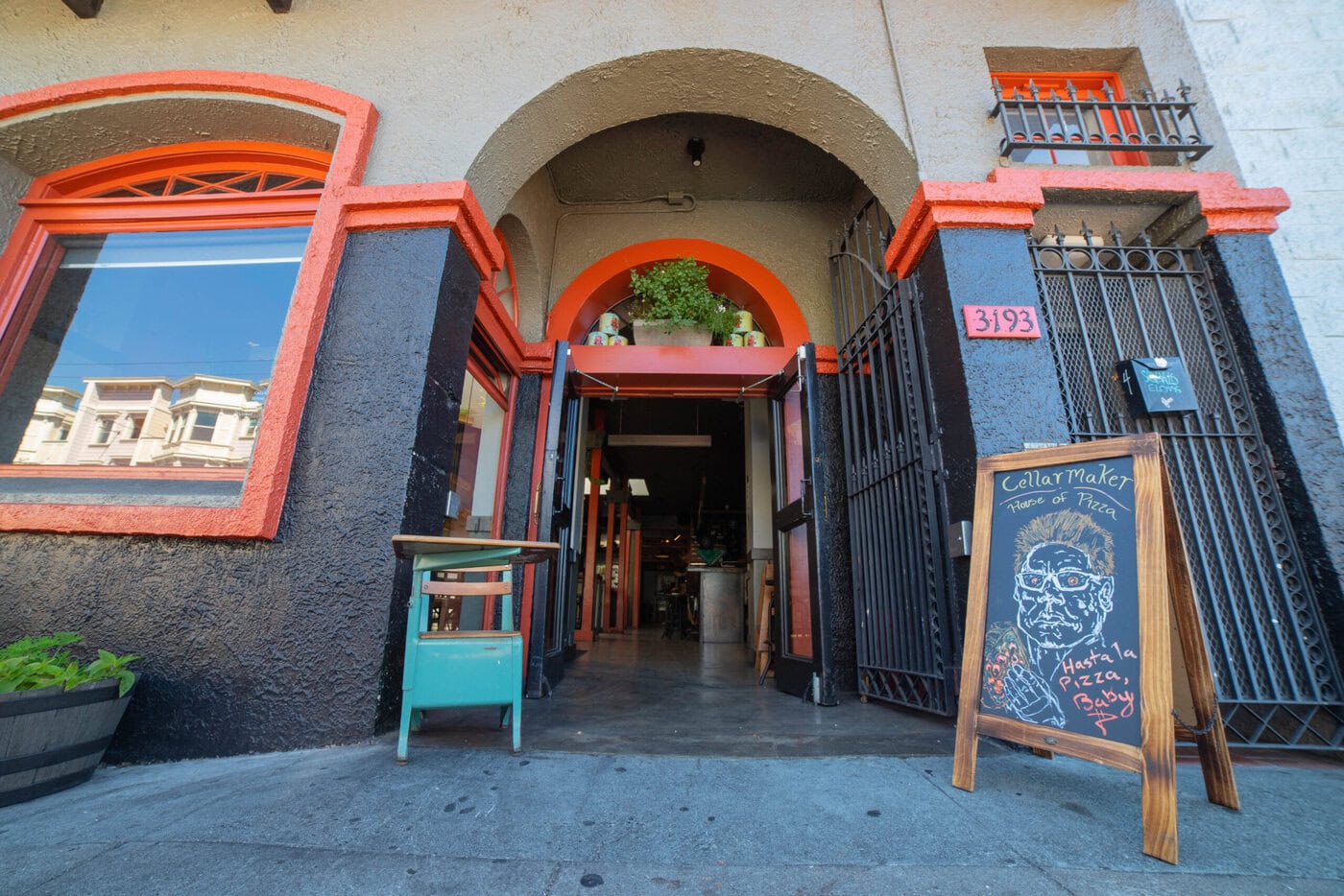 A Chalkboard Sign With A Pizza Illustration Stands Outside A Restaurant With Red And Black Trim, An Open Doorway, Arched Windows, And The Address 3193 Visible Above The Entrance.