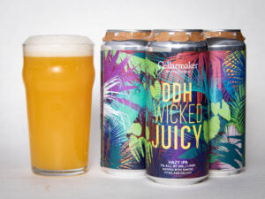 A pint glass of hazy, golden beer sits next to a four-pack of colorful cans labeled "Foreign Object - WC IPA - TDNE Collab," each featuring vibrant, tropical-inspired artwork.