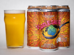 A pint glass of hazy yellow beer sits beside a four-pack of colorful cans labeled "Foreign Object - WC IPA - TDNE Collab," featuring vibrant orange artwork with a hop in a sizzling pan.