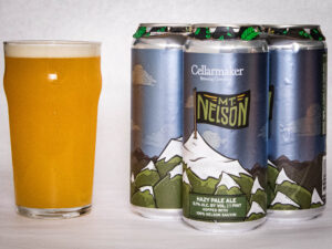 A glass of hazy pale ale sits beside four cans of Mt. Nelson - Hazy Pale Ale, each featuring a mountain illustration on the label.