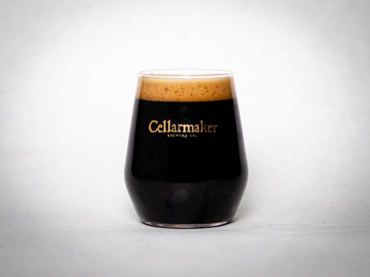 A Black Meridian Skull Glass Filled With Dark Beer And A Thick, Creamy Tan Head Sits On A White Background. The Glass Bears The &Amp;Quot;Cellarmaker Brewing Co.&Amp;Quot; Label In Gold Letters.