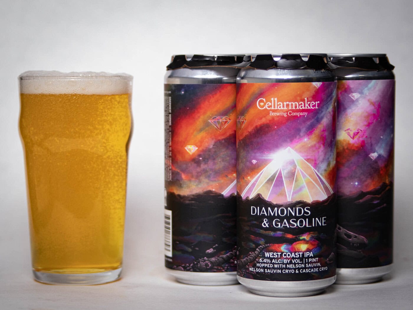 A Pint Glass Of Golden Beer Sits Next To Four Cans Of Cellarmaker Brewing Company’s Diamonds &Amp;Amp; Gasoline West Coast Ipa, Featuring Colorful Artwork With Pyramids, Diamonds, And A Cosmic Background.