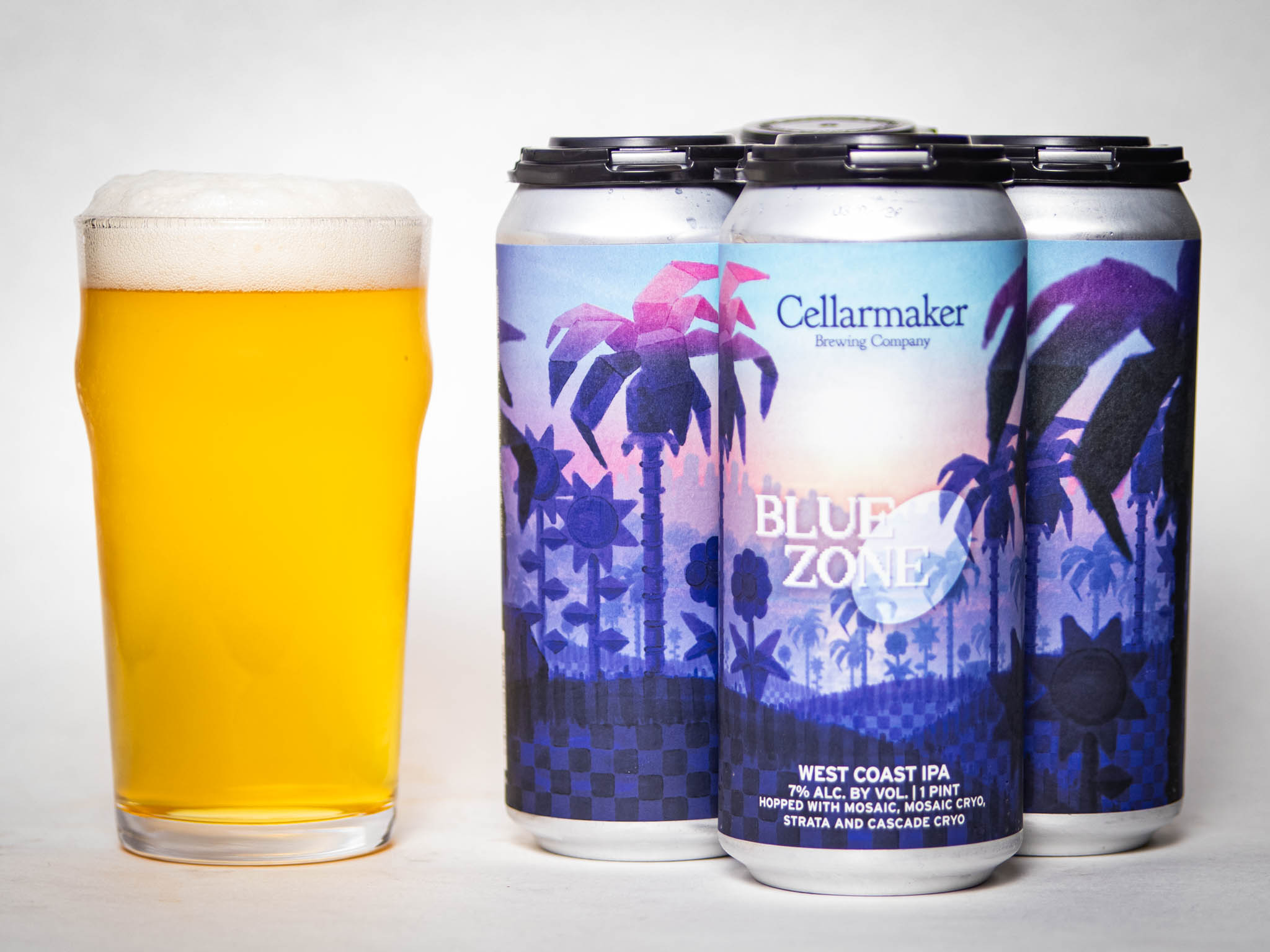 A Pint Glass Filled With Hazy Golden Beer Sits Beside Four Cans Of Cellarmaker Brewing Company’s Blue Zone West Coast Ipa, Featuring Colorful, Tropical-Themed Labels With Palm Trees And A Sunset.