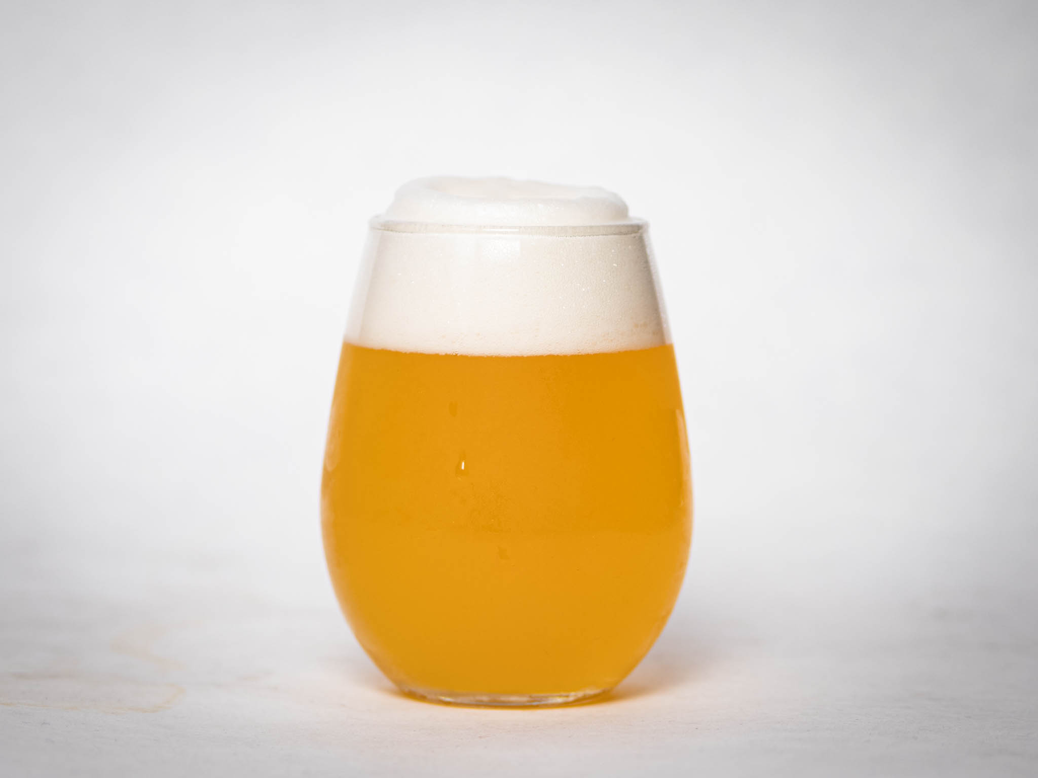 A Rounded Glass Filled With Hazy Golden Beer, Topped With A Thick, Foamy White Head, Set Against A Plain White Background.