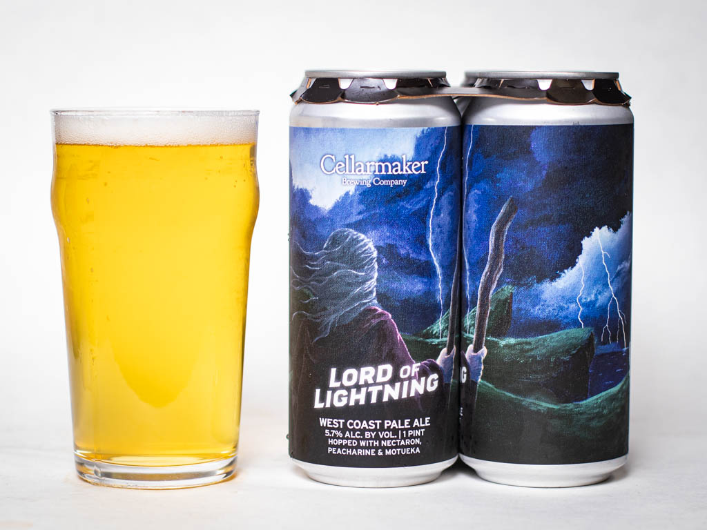 A Pint Glass Filled With Pale Yellow Beer Stands Next To Two Cans Of Cellarmaker Brewing Company’s &Amp;Quot;Lord Of Lightning&Amp;Quot; West Coast Pale Ale, Featuring Artwork Of A Figure Summoning Lightning Against A Stormy Sky.