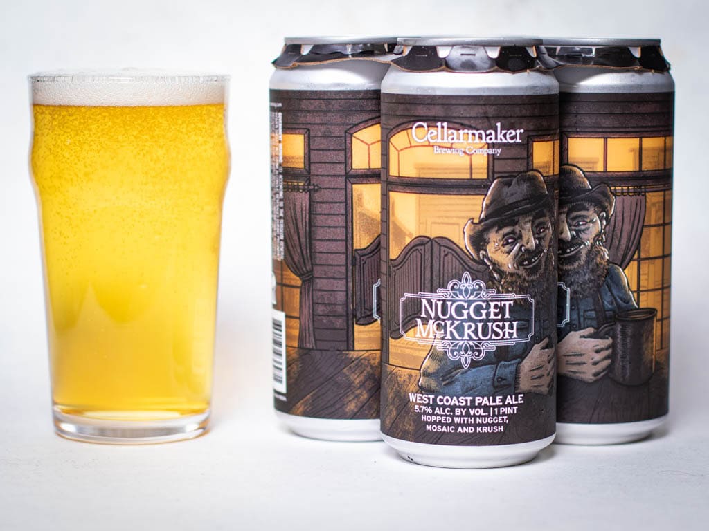 A Glass Of Pale Yellow Beer Sits Next To Three Cans Of Cellarmaker Brewing Company'S Nugget Mckrush West Coast Pale Ale, Featuring Illustrated Bearded Men On The Label In Front Of A Lit House.