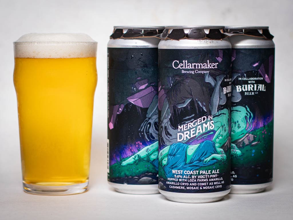 A Glass Of Hazy Pale Yellow Beer Sits Next To Three Cans Of Cellarmaker Brewing Company’s “Merged In Dreams” West Coast Pale Ale, Featuring Colorful, Abstract Artwork On The Cans.