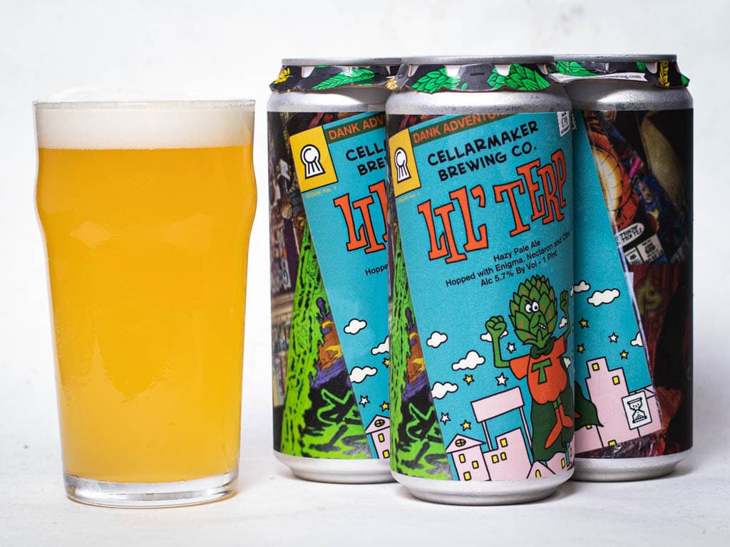 A Pint Glass Of Hazy, Pale Yellow Beer Sits Beside Three Colorful Cans Of Lil Terp - Hazy Pale Ale From Cellarmaker Brewing Co., Each Featuring A Cartoon Hop Character On The Label.