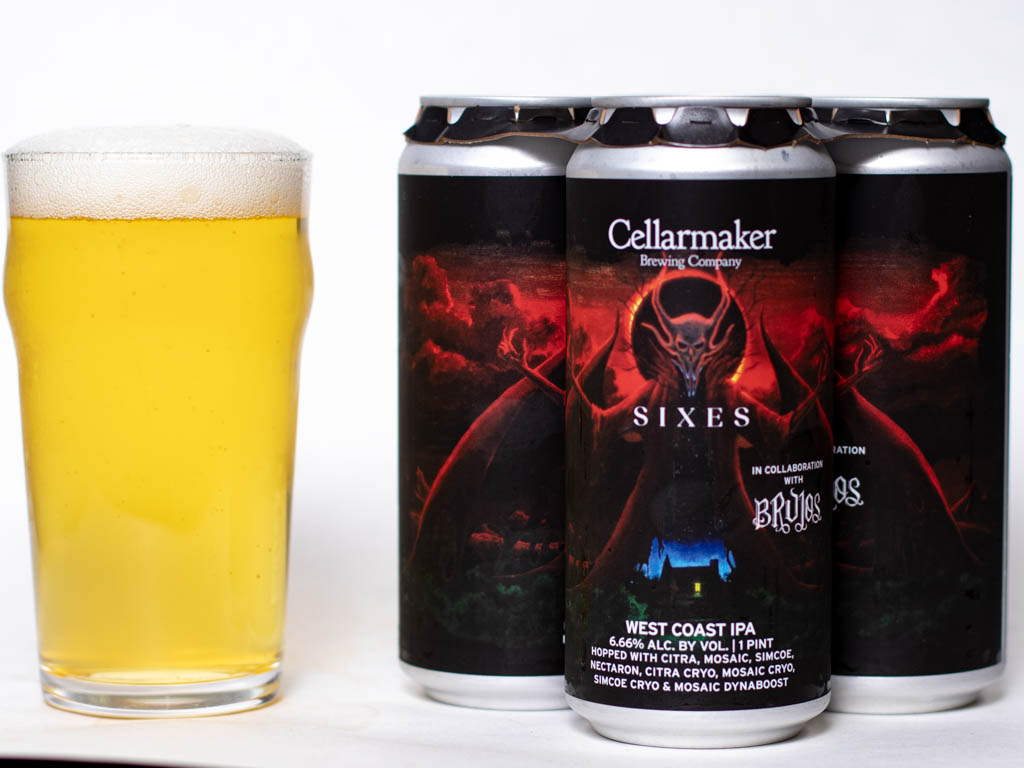 A Pint Glass Of Pale, Hazy Beer Sits Next To A Four-Pack Of Cellarmaker Brewing Company &Amp;Quot;Sixes&Amp;Quot; West Coast Ipa Cans, Featuring Dark, Dramatic Artwork With A Red Demon-Like Figure.