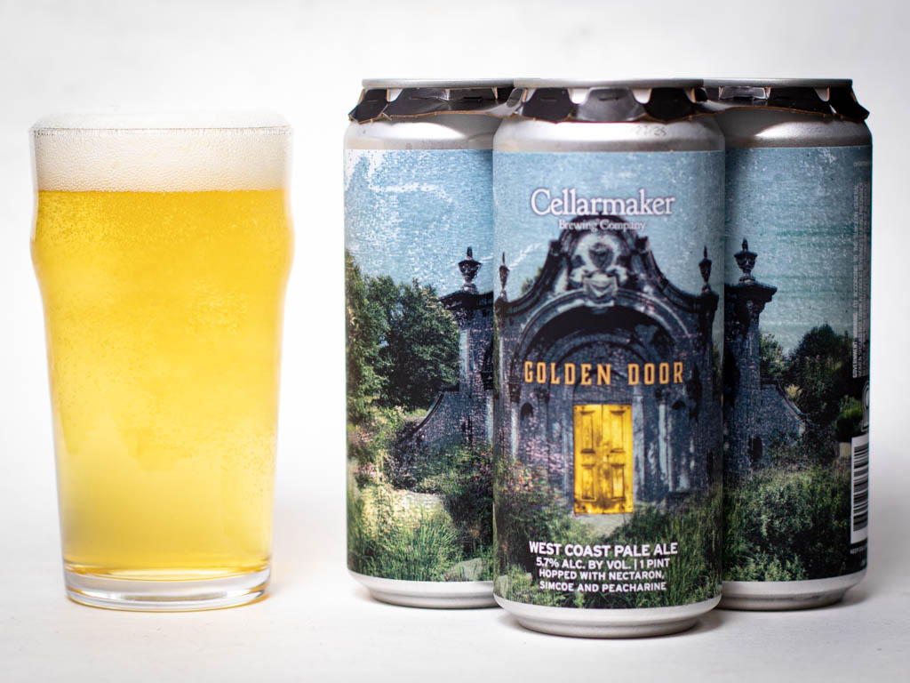 A Pint Glass Of Pale Yellow Beer Sits Next To Three Cans Labeled “Cellarmaker Golden Door West Coast Pale Ale,” Featuring A Rustic Door Surrounded By Greenery On The Label.