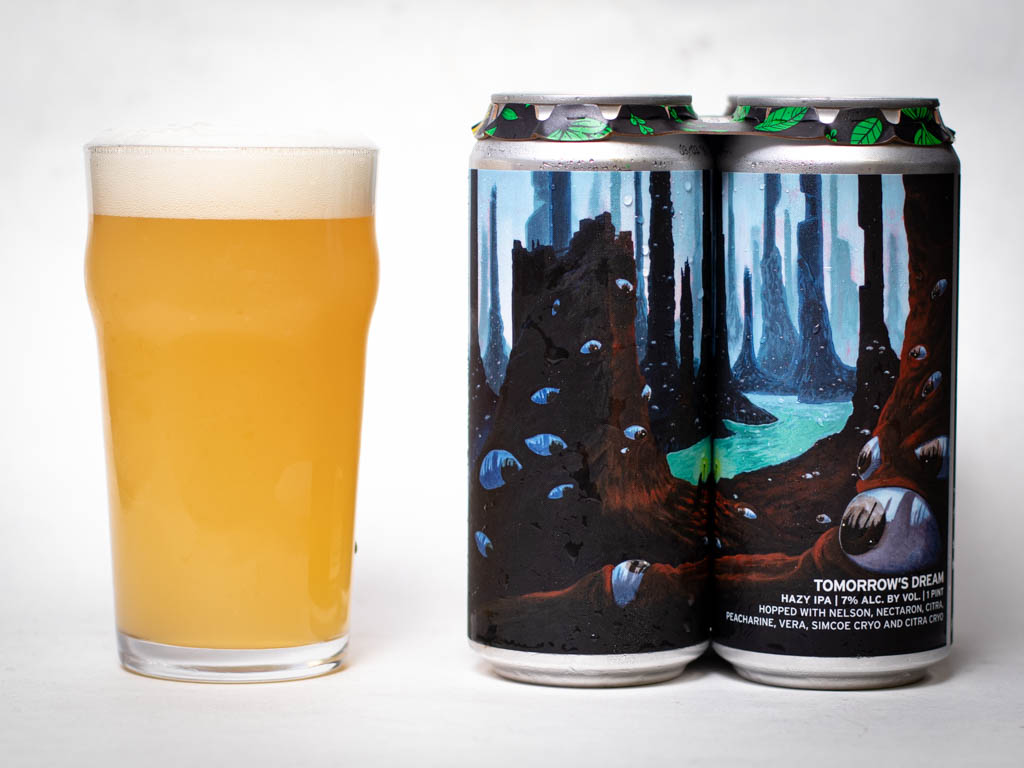 A Hazy, Pale Beer In A Glass Next To Two Cans With Colorful, Fantasy-Style Artwork Depicting A Forest Landscape With Blue Rocks And A Glowing Green River.
