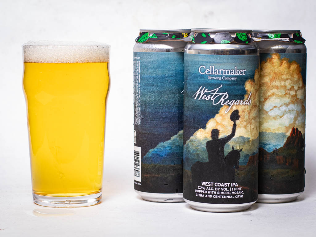 A Glass Of Hazy Golden Beer Sits Next To Three Cans Of Cellarmaker Brewing Company’s West Coast Ipa, Featuring A Label With Artwork Of People Waving In Front Of A Scenic Sky And Mountains.