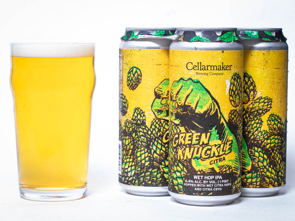 A Pint Glass Of Pale Beer Sits Next To Three Cans Of Green Knuckle Citra Ipa By Cellarmaker Brewing Co., Featuring A Green Fist With Hops On A Yellow Background.