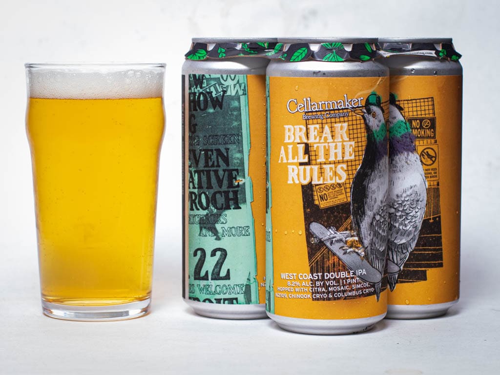 A Glass Of Light Amber Beer Sits Next To Three Cans Labeled “Break All The Rules” By Cellarmaker, Featuring A Detailed Pigeon Illustration And Bold Yellow And Green Design Elements.