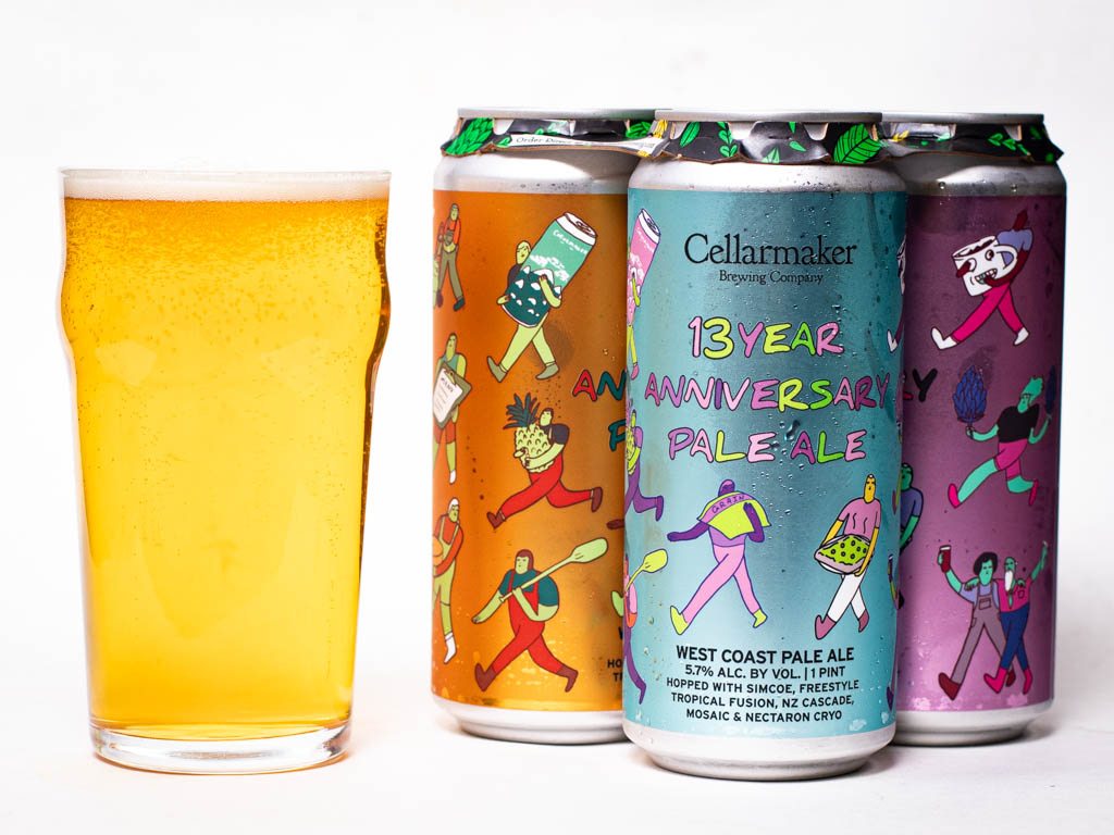 A Glass Of Pale Ale Next To A Four-Pack Of Cellarmaker Brewing Company 13 Year Anniversary Pale Ale Cans.