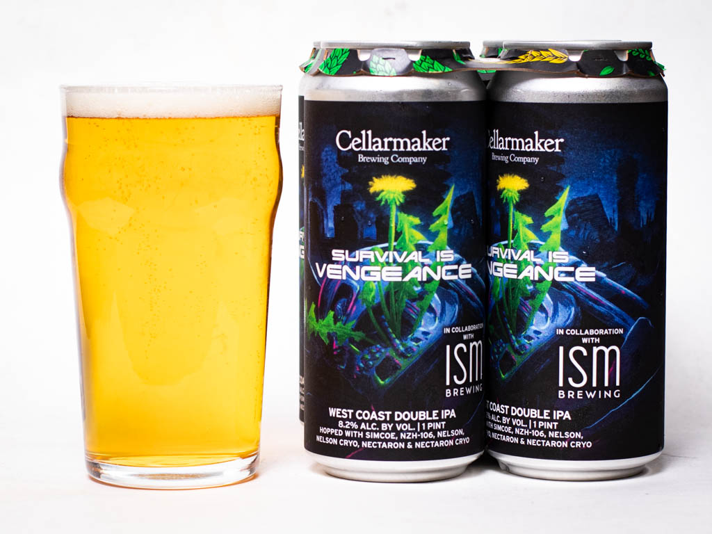 A Pint Glass Filled With Pale Golden Beer Next To Two Cans Of Cellarmaker Survival Is Vengeance West Coast Double Ipa.