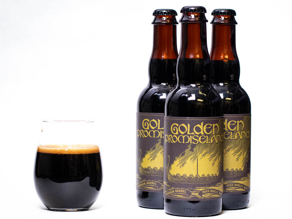 Three Bottles Of Golden Promiseland Bourbon Barrel-Aged Barley Wine Next To A Glass Of Dark Beer.