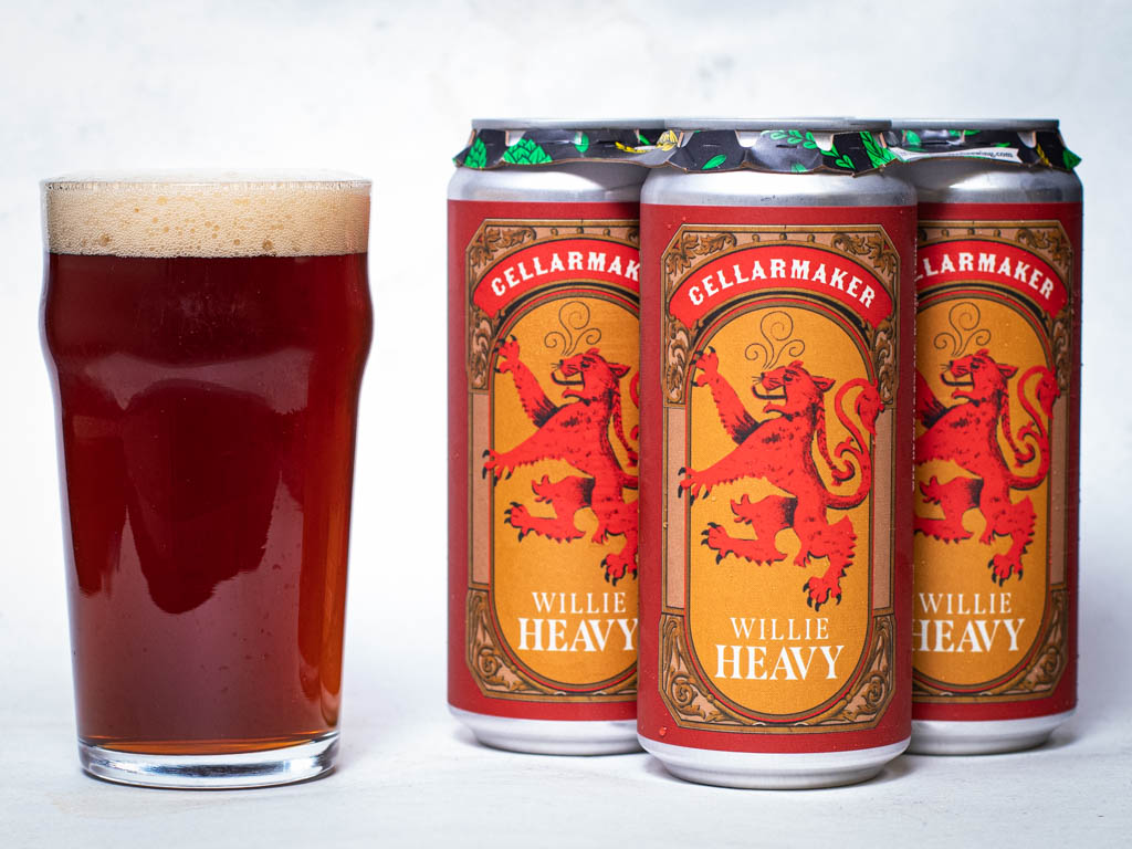 A Glass Of Amber Beer With Foam Next To A Three-Pack Of Cellarmaker Willie Heavy Beer Cans, Each Featuring A Red Lion Illustration.
