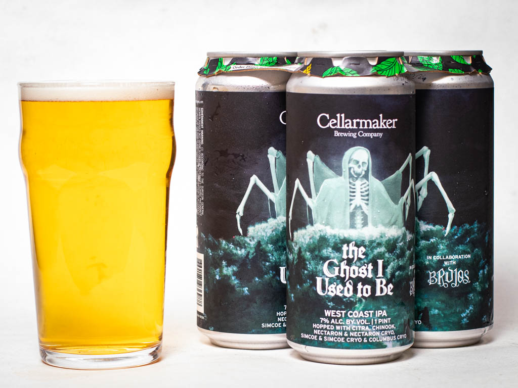A Glass Of Golden Beer Next To Three Cans Of Cellarmaker Brewing Company’s The Ghost I Used To Be West Coast Ipa.